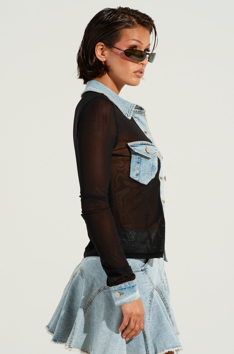 A person models the MIXED VIBES BUTTON DOWN BLOUSE, showcasing a sheer mesh design with denim accents, including a denim collar and front pockets. The outfit is paired with a light blue denim skirt, enhancing its dynamic appeal against the plain backdrop. Sunglasses provide an additional touch of style to complete the look.