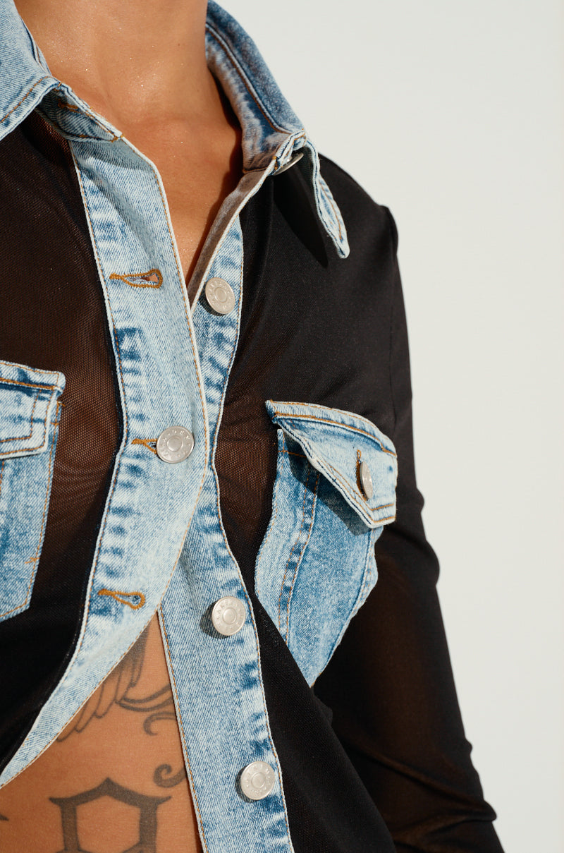Close-up of an individual dressed in the MIXED VIBES BUTTON DOWN BLOUSE from AKIRA Label, highlighting its sheer black mesh with denim highlights. This blouse showcases light blue washed denim pockets and front button closure, offering a glimpse of a tattoo underneath and exuding eclectic charm through its contrasting materials.