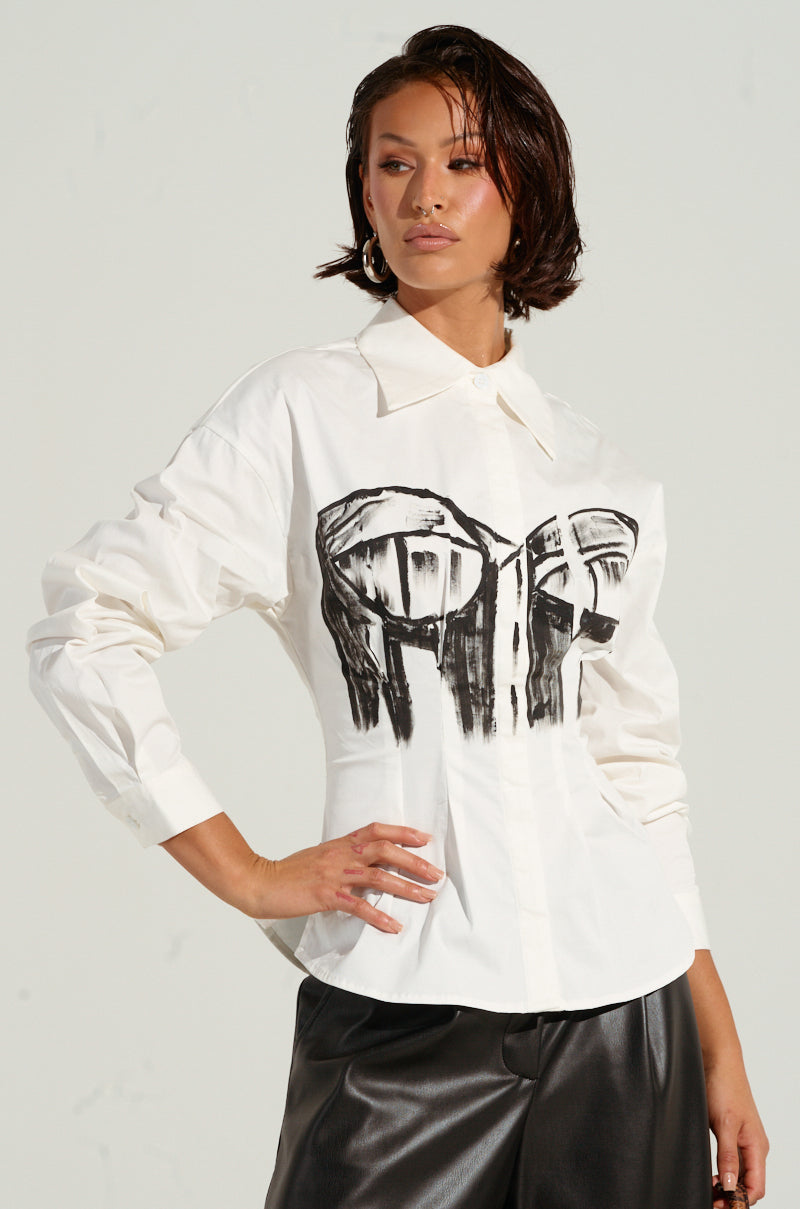 A person wearing the BAD FOR YOU BUTTON DOWN BLOUSE, featuring bustier-inspired graphic designs on the front, paired with black leather pants. They are posing with one hand on their hip against a plain background.