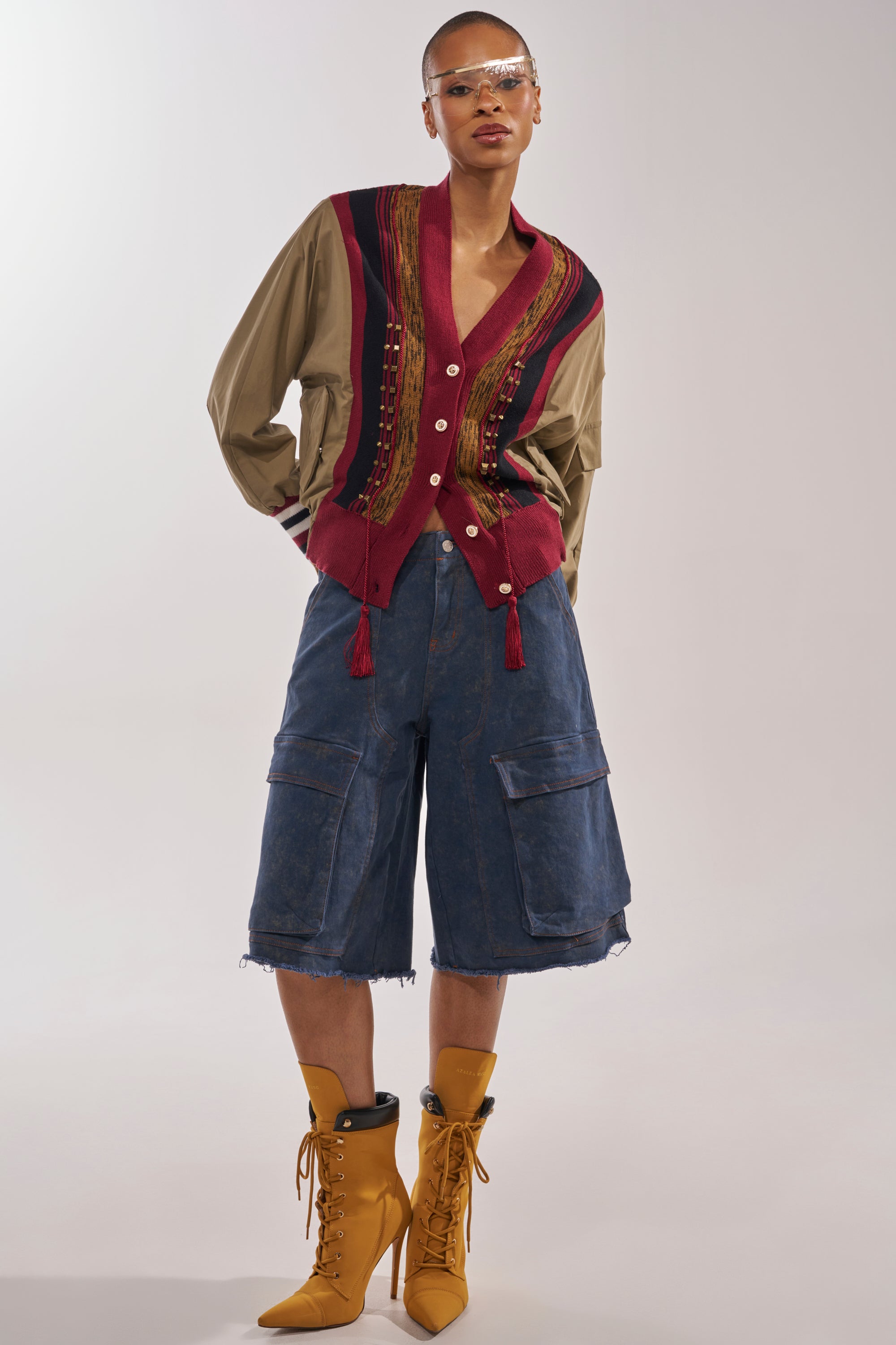 A person wearing clear visor glasses, a tan shirt layered with the NEW DAY COLORBLOCK CARDIGAN, oversized blue cargo shorts, and tan lace-up heeled boots stands against a plain background. 7