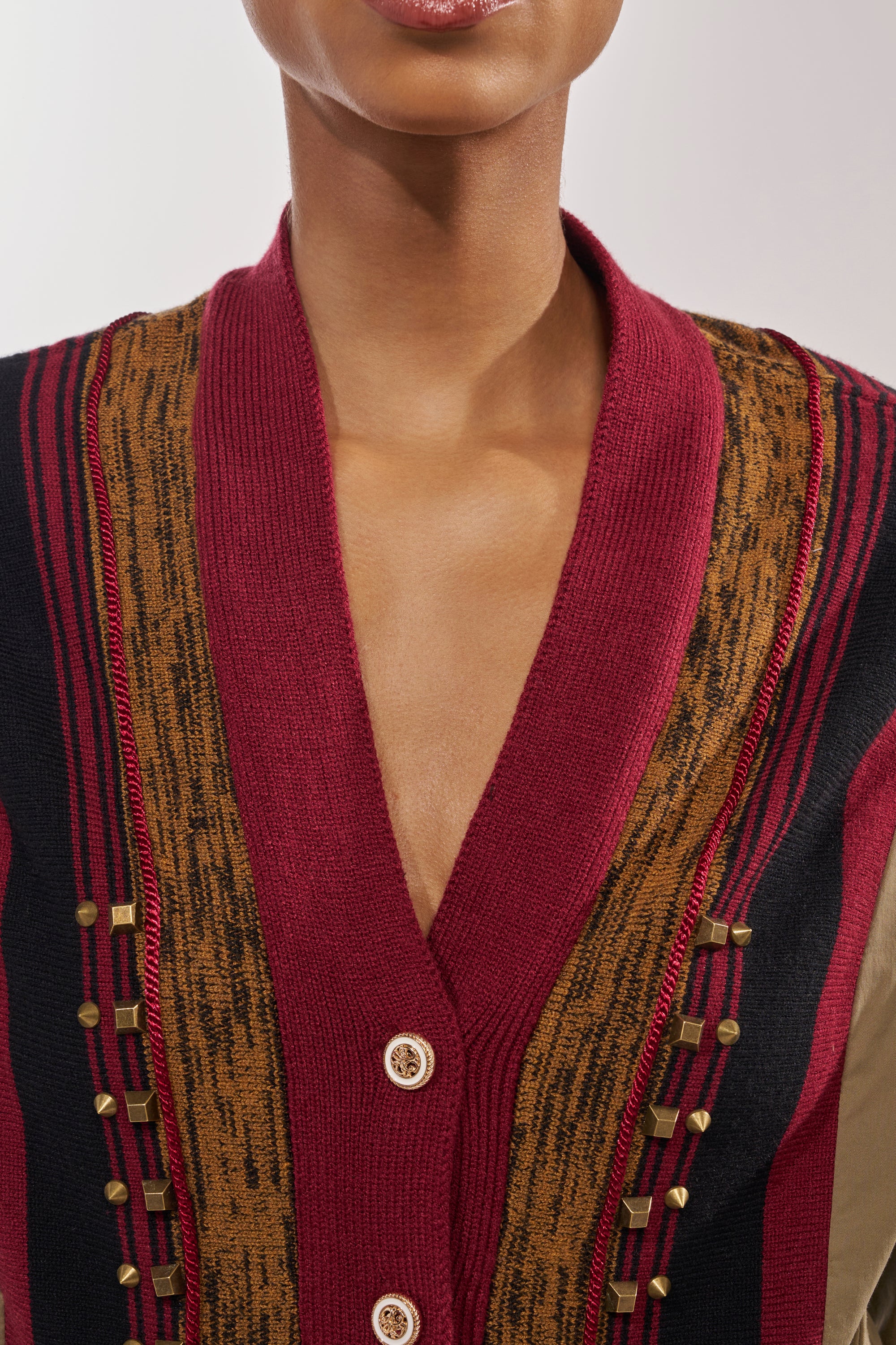 A close-up of a person wearing the NEW DAY COLORBLOCK CARDIGAN with maroon, brown, and black patterns, decorative stitching, and gold studs; only the lower face, neck, and upper chest are visible. 8