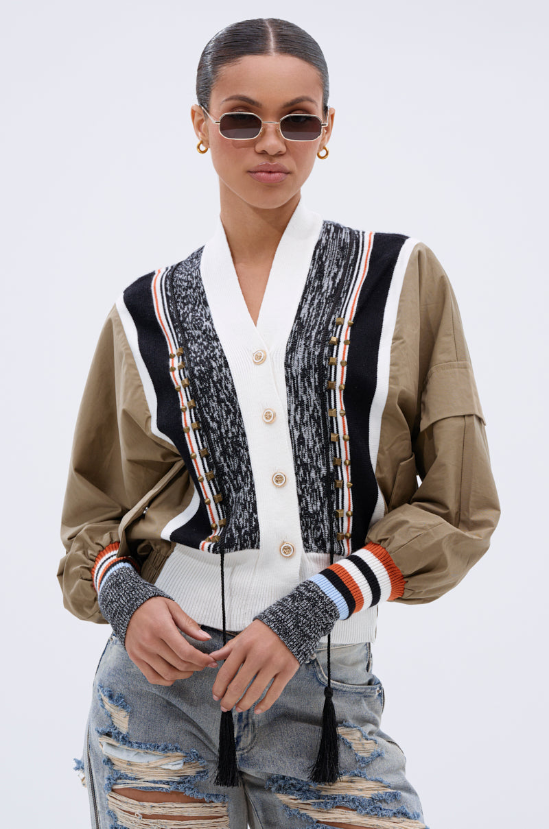 A woman wearing sunglasses, gold hoop earrings, ripped jeans, and the BEAUTIFUL DAY CARDIGAN over a tan shirt stands confidently against a plain white background.
