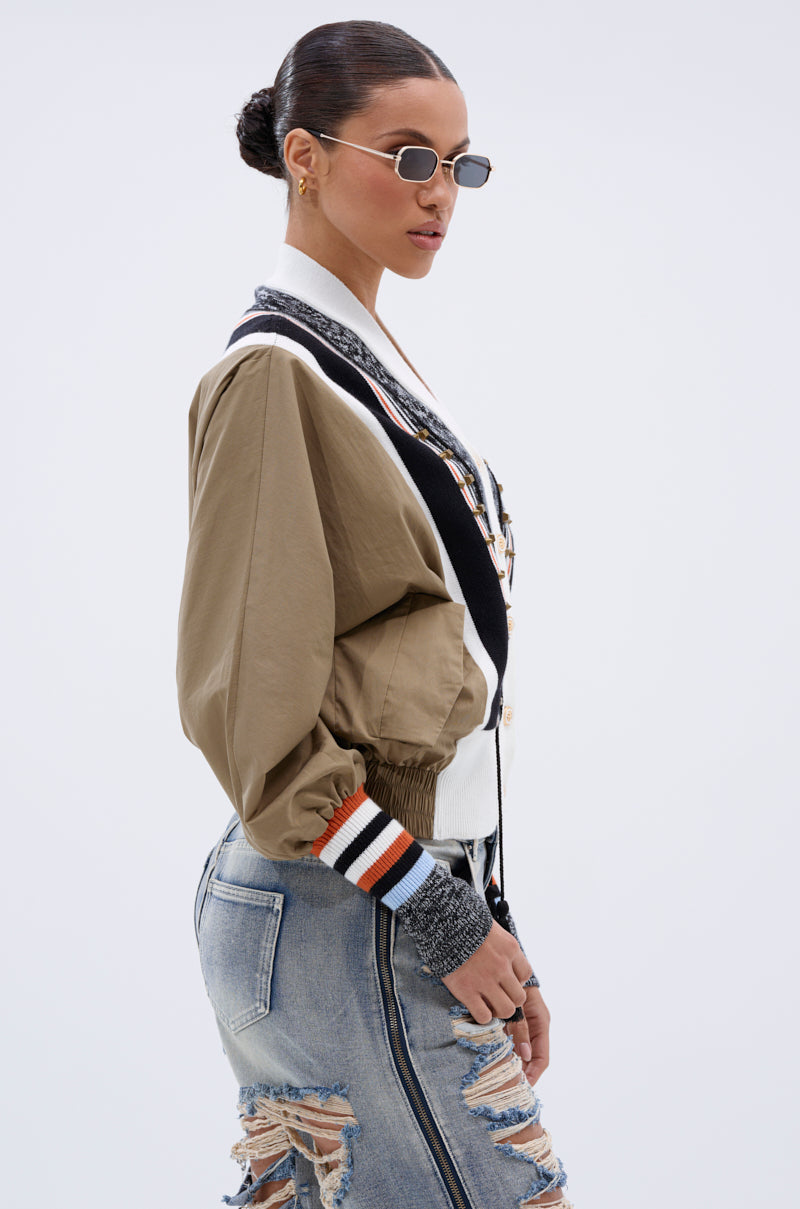 A woman with slicked-back hair wears the BEAUTIFUL DAY CARDIGAN, oval sunglasses, gold hoop earrings, and distressed denim jeans as she stands in profile against a plain white background.