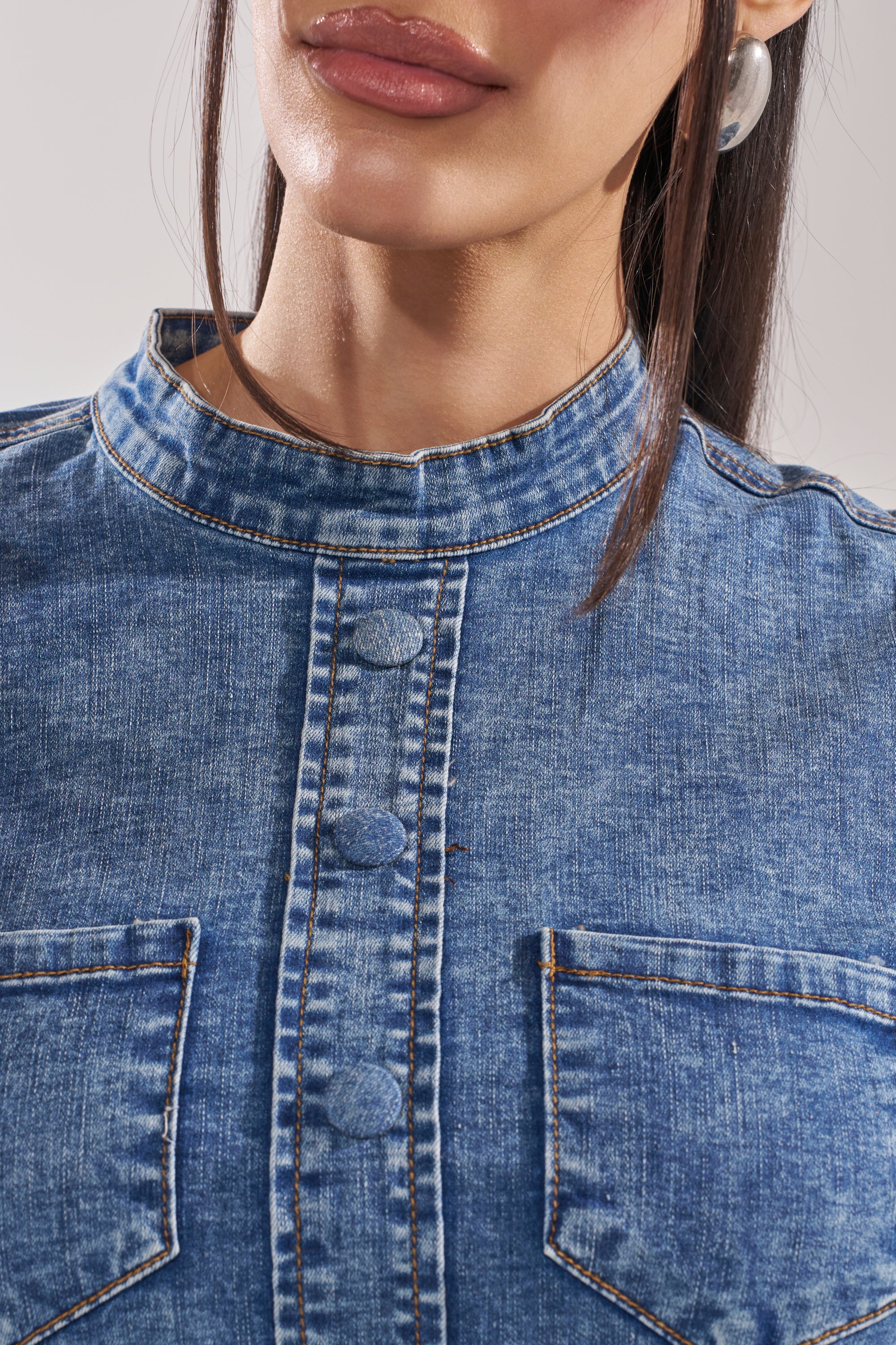 Close-up of a woman wearing the SEIZE THE DAY LONG SLEEVE FLOUNCE MEDIUM BLUE DENIM TOP, featuring a mandarin collar, button placket, and chest pockets; only her lower face and upper torso are shown.