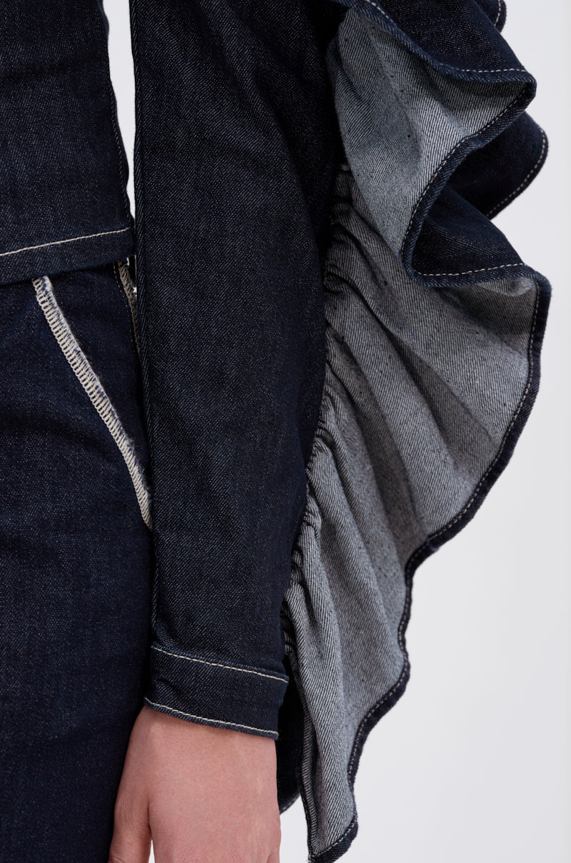 A close-up shows someone wearing the RUFFLED UP LONG SLEEVE DENIM TOP—a dark-wash denim piece with ruffle sleeves, visible light gray inner fabric, and a pocket accented by contrasting light stitching.