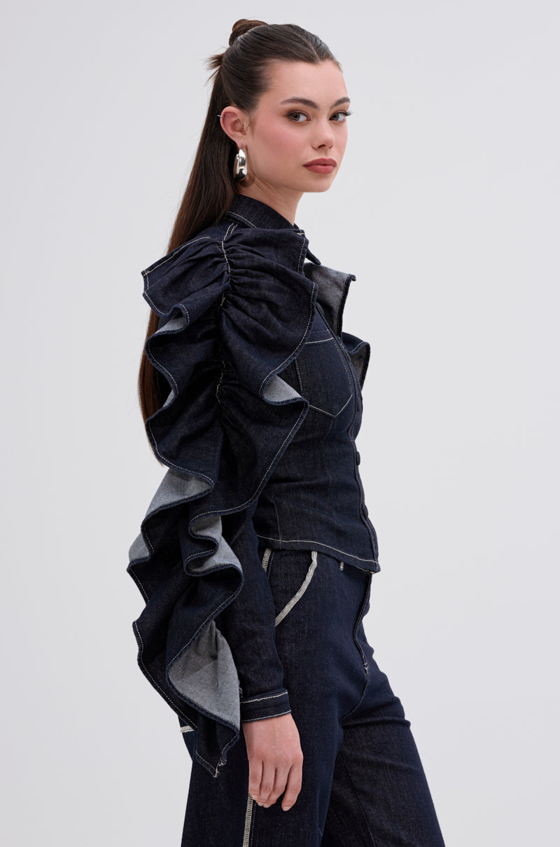 A woman with long dark hair in a high ponytail wears the RUFFLED UP LONG SLEEVE DENIM TOP, featuring dramatic ruffle sleeves, as she stands in profile against a plain light background.