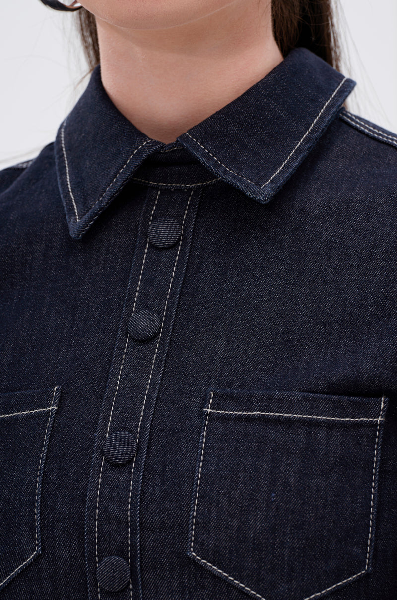 Close-up of the RUFFLED UP LONG SLEEVE DENIM TOP, featuring dark-wash denim with white stitching, two chest pockets, and fabric-covered buttons. The image highlights the collar, buttons, and upper pocket area.