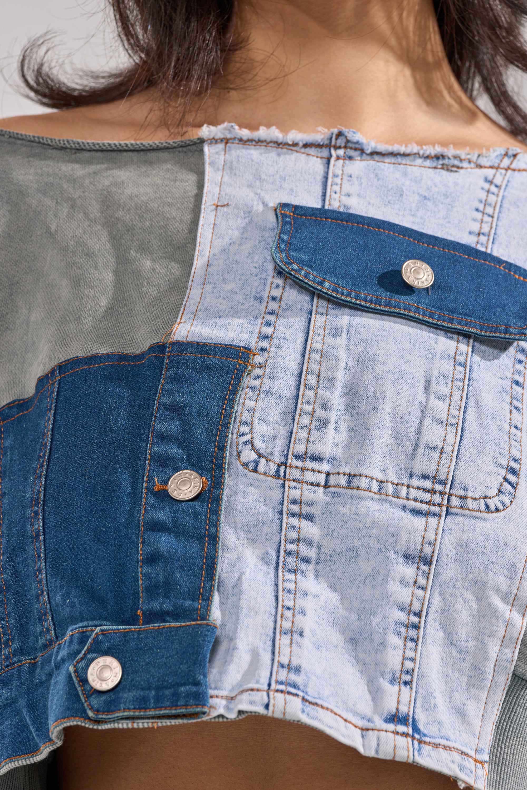 A close-up of a person wearing the DENIM DREAMS ZIPPER DETAIL SWEATSHIRT, featuring patchwork denim in various blue shades, two front pockets, zipper details, and a raw-edge neckline for a unique look.