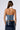 A person with long brown hair is shown from the back, wearing the CASUAL FRIDAY DENIM CORSET TOP, which features a strapless and lace-up design, paired with a shiny dark blue patent leather skirt. The background is plain white.