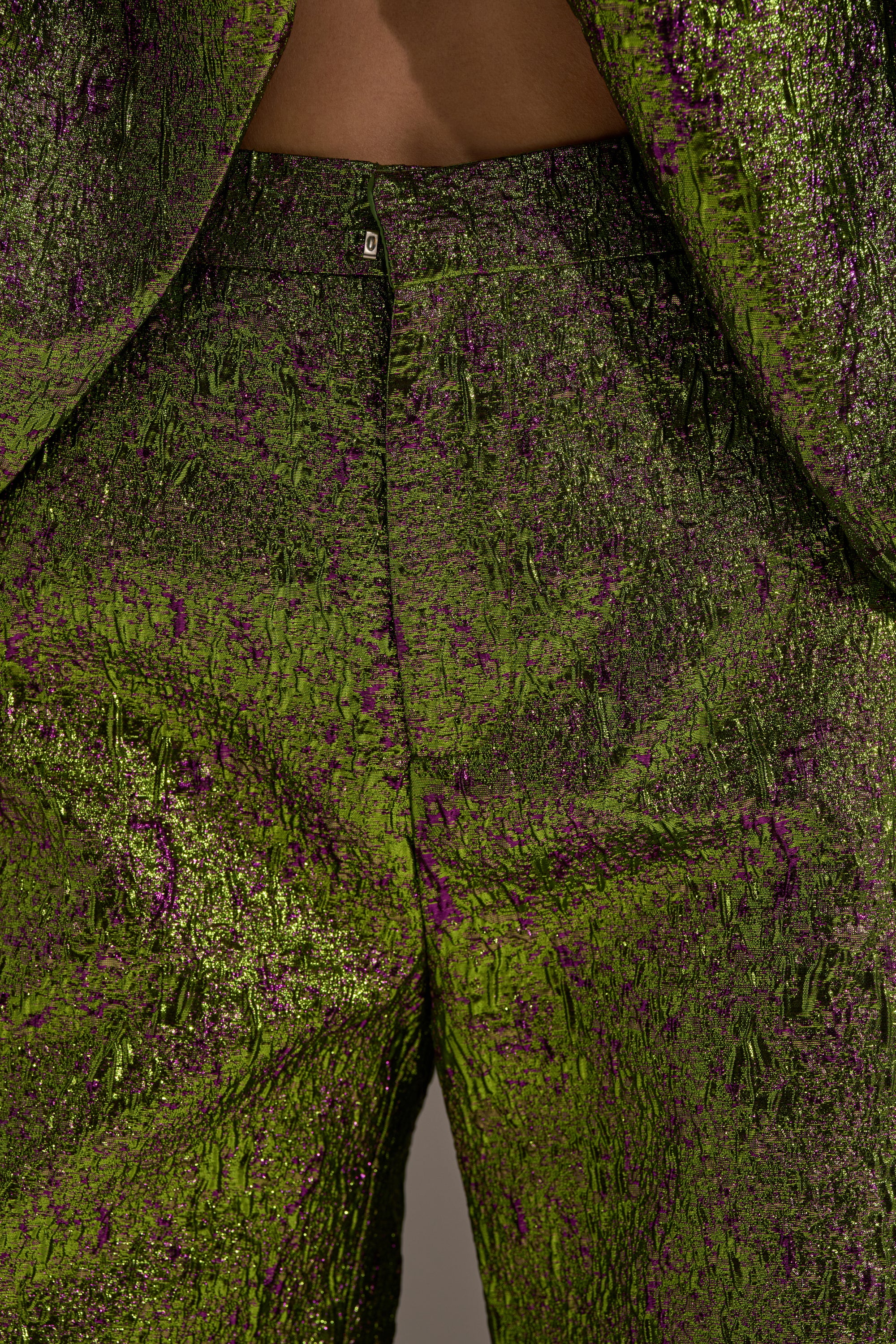 Close-up of a person wearing LAYLA BROCADE CULOTTES and a matching jacket. The shiny, crinkled green and purple fabric shows off intricate details—perfect statement pants for your next holiday party.