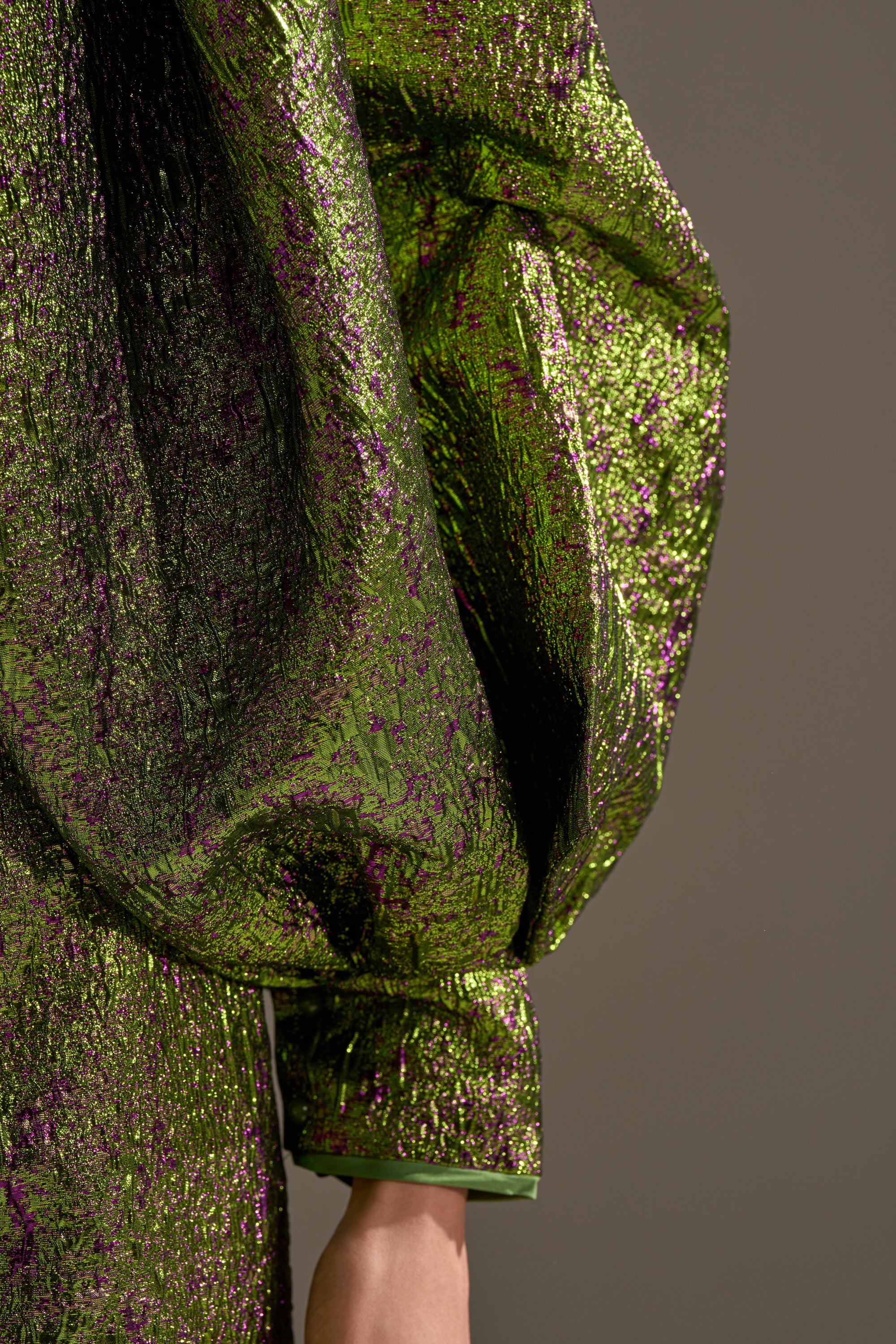 A close-up of a person wearing the LAYLA BROCADE PUFF SLEEVE MOCK NECK TOP, featuring shiny green and purple textured fabric with voluminous puff sleeves, set against a plain background.