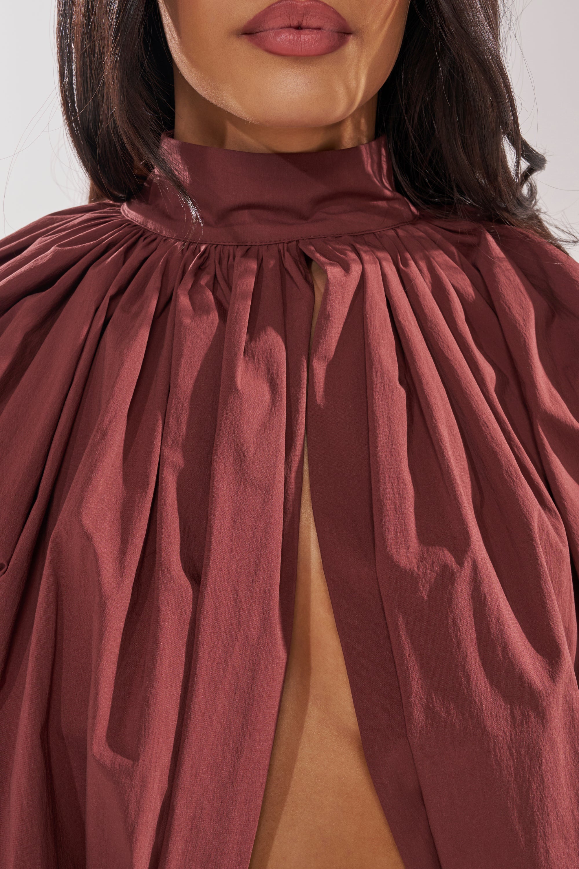 A close-up of a woman in the GOLD COAST BALLOON SLEEVE BLOUSE IN BROWN with her dark hair over her shoulders and natural makeup, highlighting modern minimalism with subtle mauve lipstick. 8