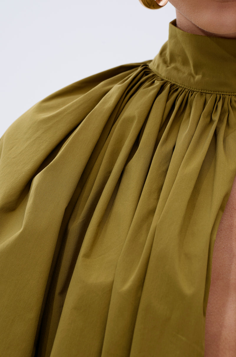 Close-up of a person wearing the GOLD COAST BALLOON SLEEVE BLOUSE in olive green, featuring gathered fabric at the collar. The image highlights the blouse's texture and detail on the upper chest and shoulder.