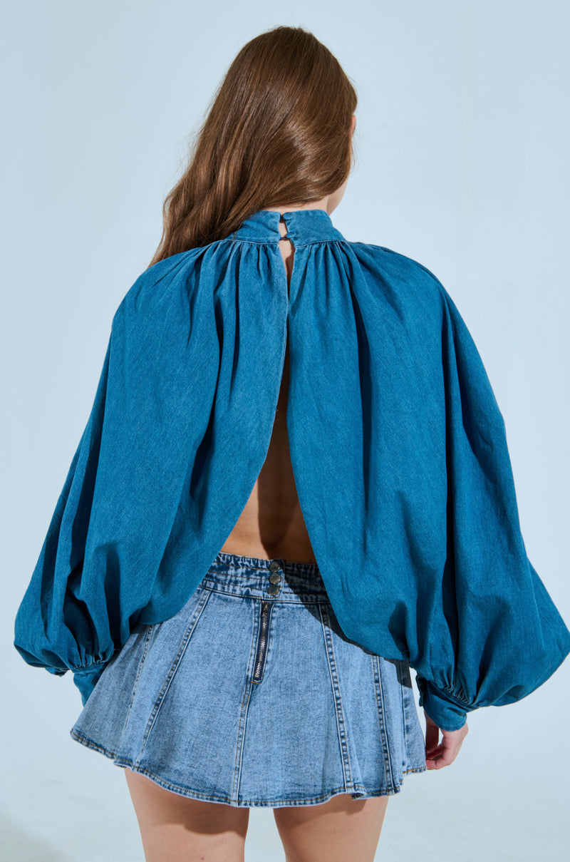 A person with long hair is facing away, wearing the MASTERPIECE MEDIUM DENIM LONG SLEEVE PUFF BLOUSE in a cropped silhouette and a short denim skirt with slight pleats. 3