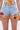 Wearing the VIVI FLORAL DENIM SHORT—high-rise denim adorned with colorful floral embroidery—and a sheer top with matching appliques creates a vibrant, playful look with orange, pink, purple, and yellow blooms and green leaves.