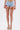 Wearing the VIVI FLORAL DENIM SHORT with embroidered floral appliques, a sheer floral top, and gold platform sandals featuring rainbow-striped soles.