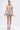 A woman stands against a plain background wearing the VIVI FLORAL DENIM SHORT, paired with a strapless sheer floral top and platform heels with colorful stripes.