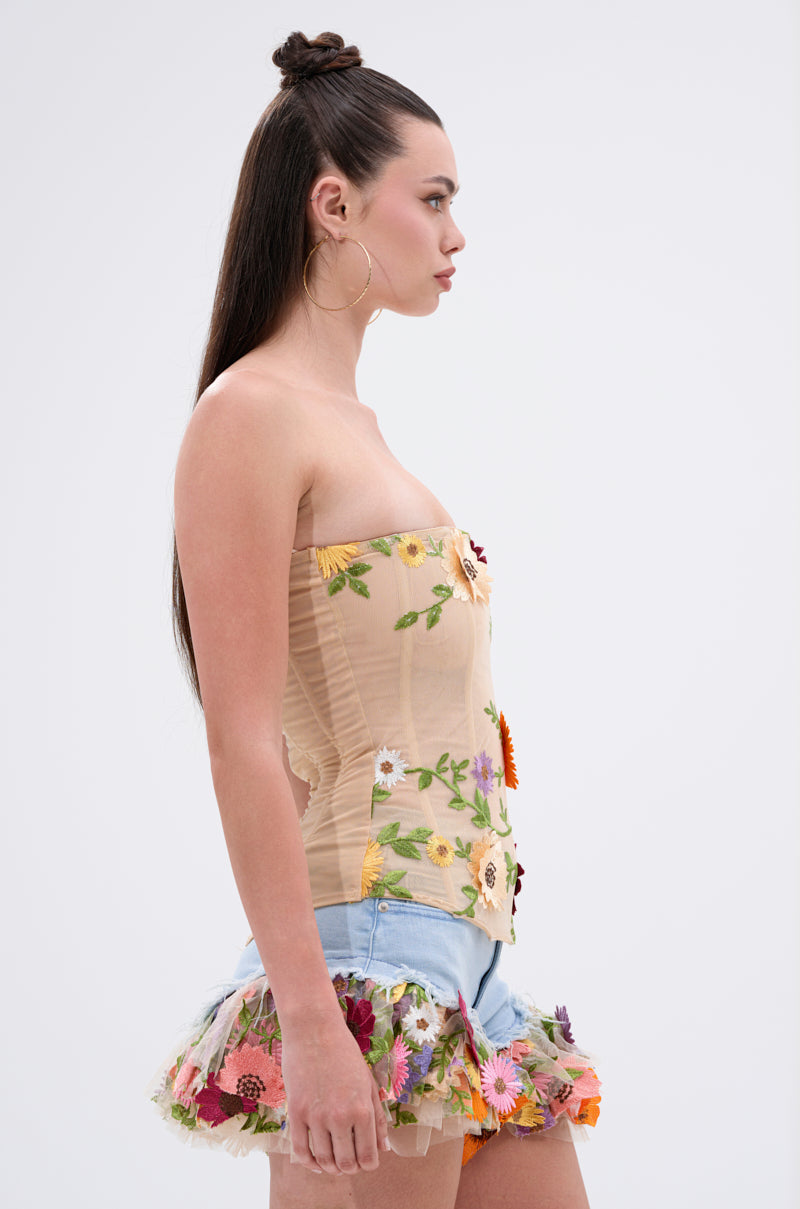 A woman with long, straight hair in a half-up style models the VIVI FLORAL CORSET with floral appliques and a mini skirt, posing in profile against a simple light background.