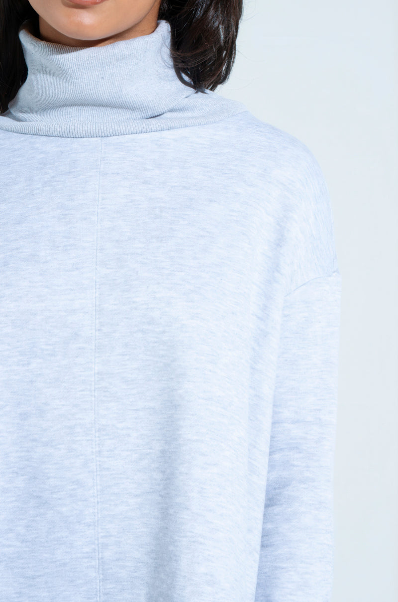 The image shows a person wearing the LAINIE TURTLENECK HIGH LOW SWEATSHIRT DRESS in light gray, focusing on the lower face and upper torso. The texture and relaxed fit of the dress are evident against a plain off-white background.