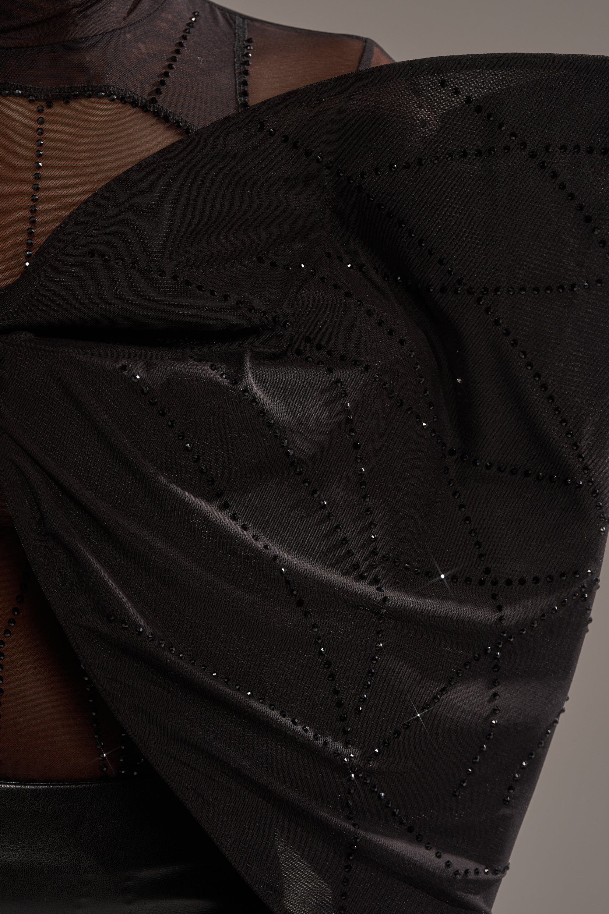 A close-up of the SPIDER GIRL BOW TOP, a sheer black top featuring a sculpted bow adorned with rhinestone geometric patterns, offering a dramatic and elegant look.