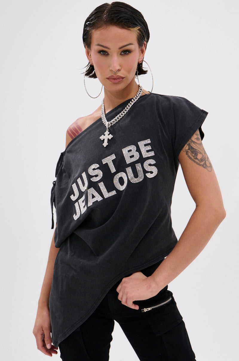Confident person with wet-look dark hair, tattoos, and hoop earrings poses in a black JUST BE JEALOUS OFF THE SHOULDER TEE, styled with a chain necklace against a plain background.