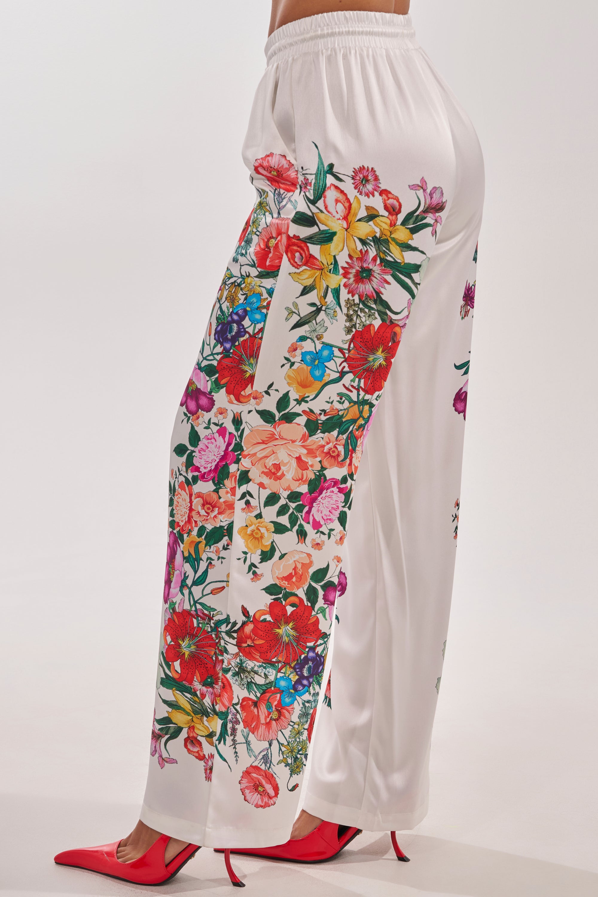 The FULL BLOOM STRAIGHT LEG TROUSERS, featuring a vibrant floral print on white satin, are styled with red pointed-toe heels—shown from the waist down against a plain background for a chic spring brunch look. 5