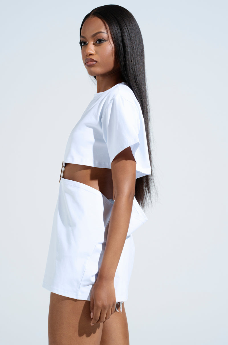 A person with long straight hair wears a Girl Boss Moments Cut-Out T-shirt and matching high-waisted shorts, exuding high-fashion drama as they stand sideways against a plain light blue background.