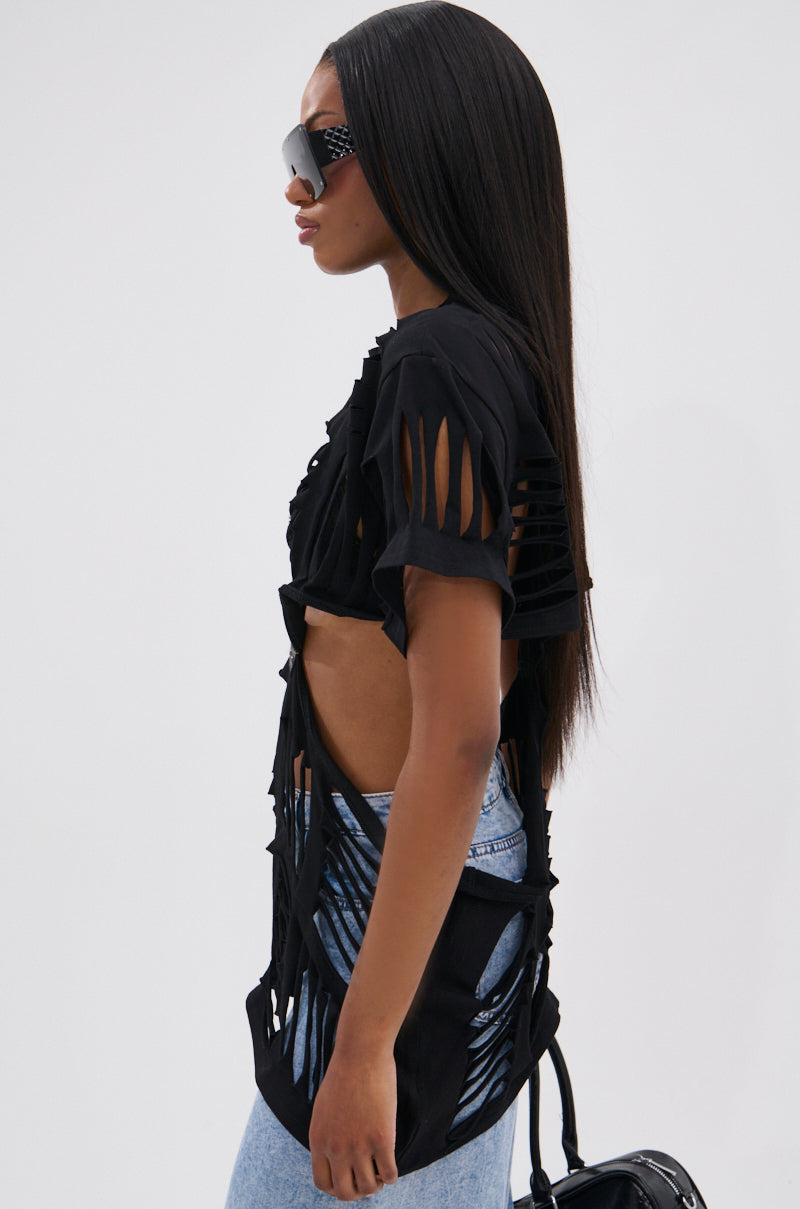 A woman in profile wears large sunglasses, light wash jeans, a small black handbag, and the SHREDDED OVERSIZED SHORT SLEEVE TEE with cut-out details. Her long, straight hair adds to her edgy grunge-inspired style.