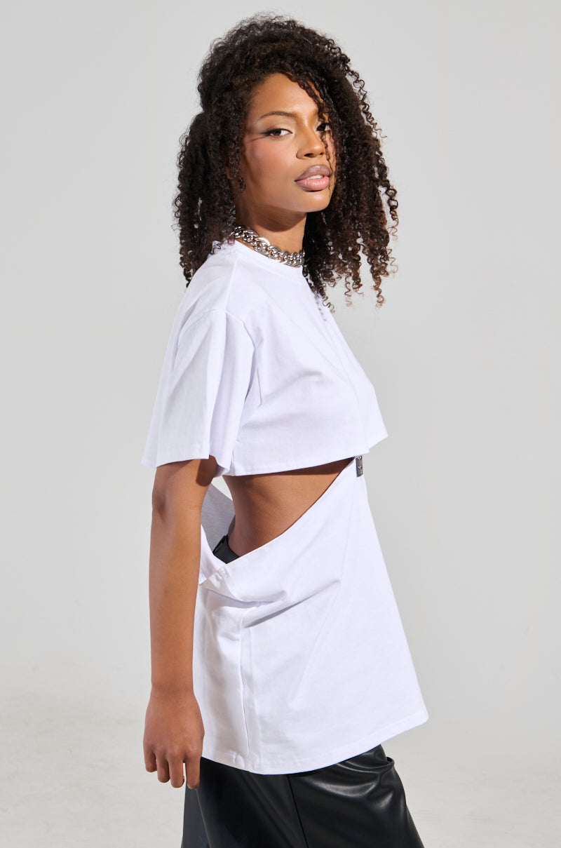 A person with curly hair sports a chic look, wearing the GIRL BOSS MOMENTS CUT OUT T-SHIRT and black pants. They stand sideways, looking towards the camera in a well-lit studio setting.
