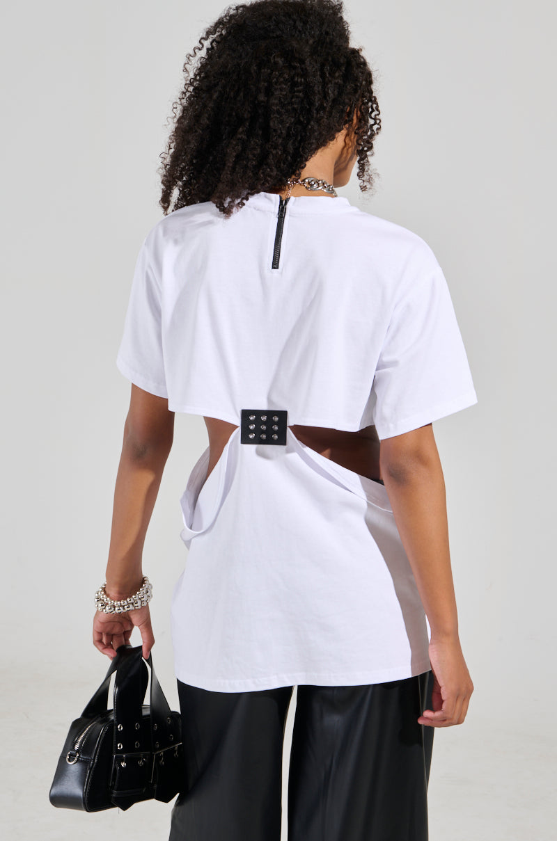 A person with curly hair stands stylishly with their back to the camera, featuring the GIRL BOSS MOMENTS CUT OUT T-SHIRT in white paired with black pants. They carry a small black handbag and add flair with bracelets on their wrist, showcasing a truly unique design.