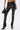 A person wears shiny black STRAIGHT TO THE POINT FAUX LEATHER LEGGING with a skinny fit and front ankle slits, paired with black pointed lace-up high-heeled boots, a small black handbag, and a wide silver cuff bracelet.