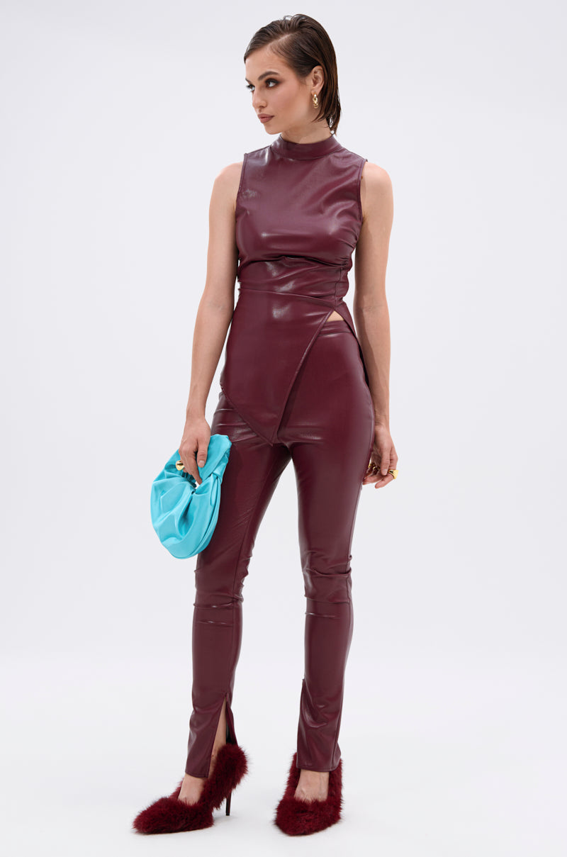 A woman wears FIRE SQUAD BURGUNDY LEGGING, styled with a sleeveless fitted burgundy faux leather jumpsuit, pointed details, furry burgundy heels, and a light blue clutch, posing against a plain white background. 8