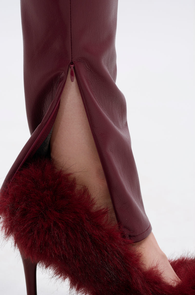 Close-up of a lower leg in the FIRE SQUAD BURGUNDY LEGGING with an open ankle zipper, revealing a high-heeled sandal featuring fluffy dark red fur. 9