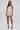 A woman stands against a plain background wearing a strapless white satin mini dress with lace-up sides inspired by the FESTIVAL GIRLY LACE UP MINI SKIRT, paired with white high-heeled sandals and a small white handbag.