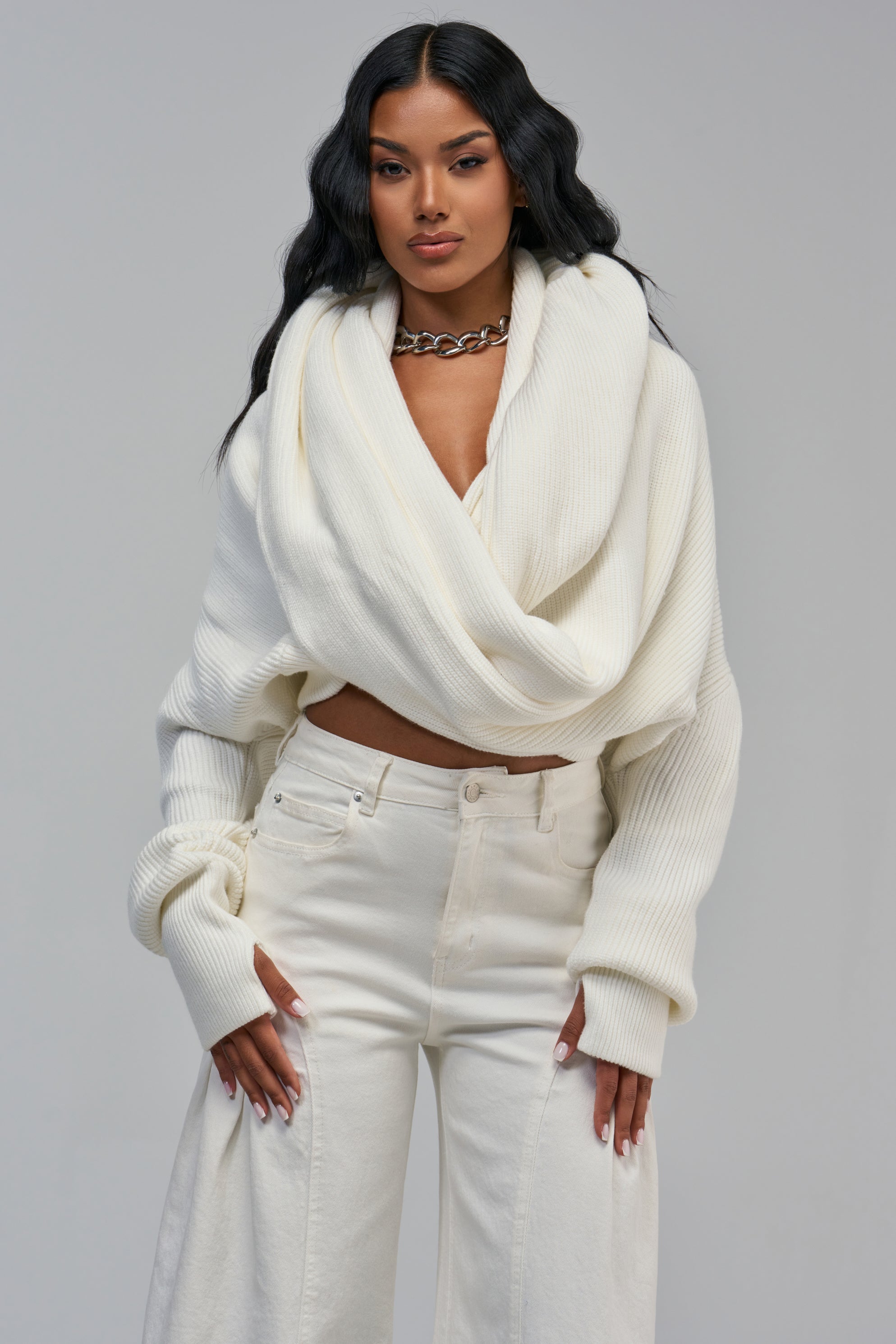 A woman wearing a JUST TOO COOL FOR YOU SWEATER, a cozy chunky white knit wrap sweater with long sleeves, paired with light-colored jeans.