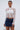 A woman models the GIMME MORE LACE ZIP-UP TOP over a white bandeau and blue denim mini skirt, holding a small white handbag against a plain light background.