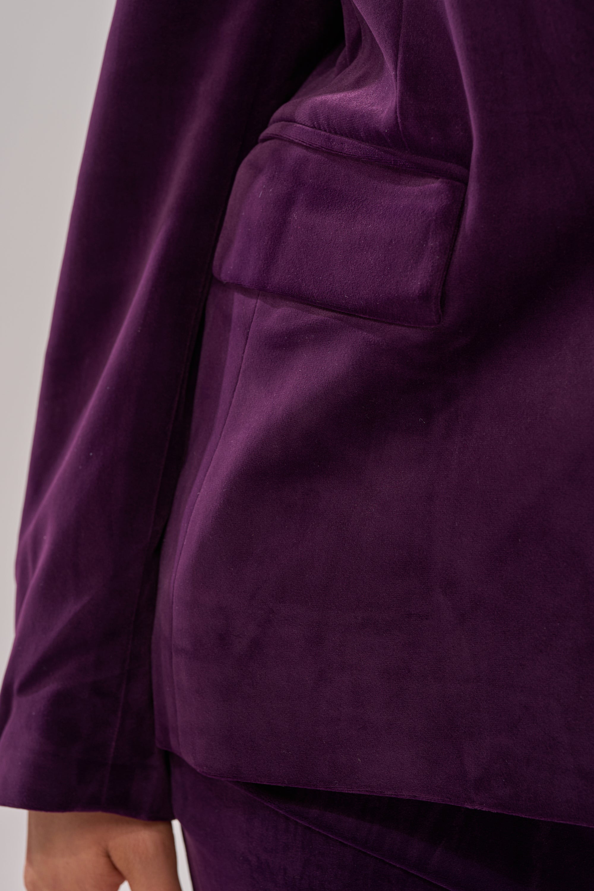 Close-up of a person wearing the I ADORE YOU BLAZER in plum purple velvet, highlighting the pocket and arm area, with the soft texture of the fabric clearly visible.