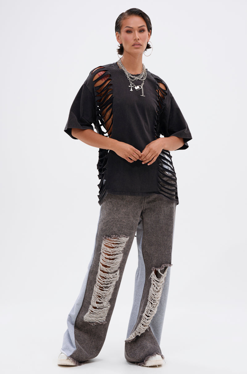 A person stands confidently in the SHAINA DISTRESSED OVERSIZED TEE with cutout details, paired with loose, two-tone ripped jeans and white sneakers. 5