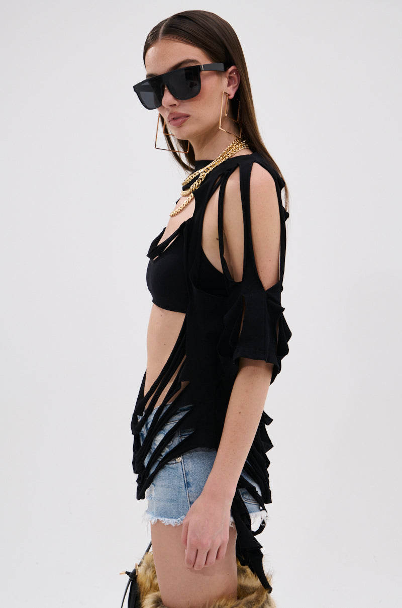 A woman wears the NOTHING THERE DISTRESSED TEE over a black bra, paired with denim shorts and furry boots, accessorized with sunglasses and gold jewelry, standing against a plain white background.