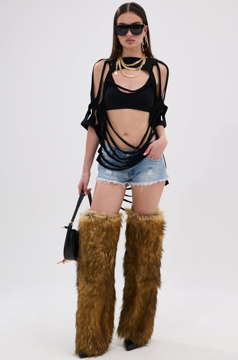A woman poses in the NOTHING THERE DISTRESSED TEE, styled with denim shorts, gold chains, sunglasses, tall brown furry boots, and a black purse against a plain light background.