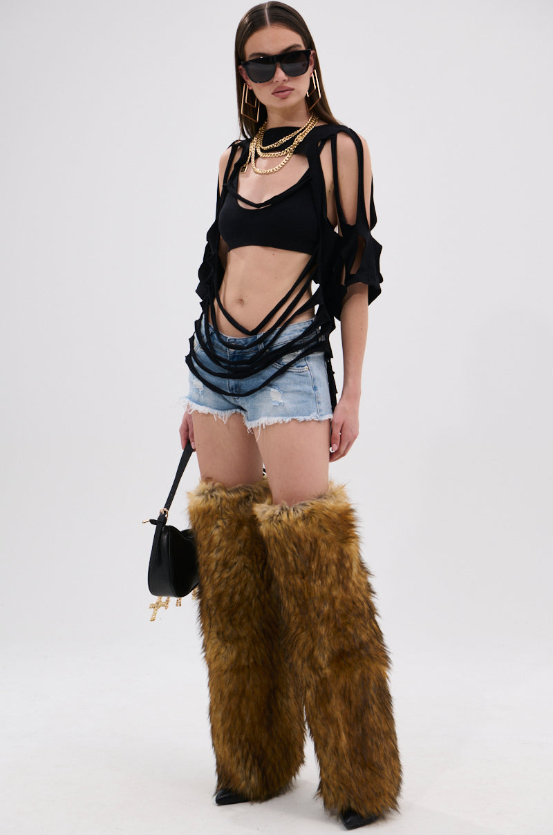 A woman in sunglasses wears the NOTHING THERE DISTRESSED TEE, layered necklaces, distressed denim shorts, and furry brown leg warmers. She holds a black handbag with gold accents against a white background for a deconstructed look.