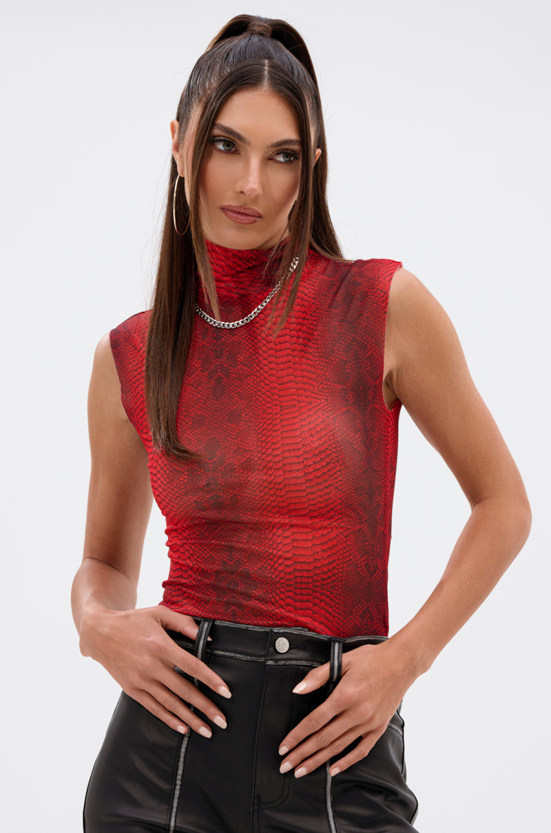 Woman with long brown hair in a high ponytail wears the SEXY LITTLE SNAKE MESH TOP IN RED, paired with black leather pants, large hoop earrings, and a silver chain necklace, standing against a plain light background. 0