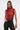 A woman with long brown hair in a high ponytail wears the SEXY LITTLE SNAKE MESH TOP IN RED, paired with black high-waisted pants with white stitching and a silver chain necklace, standing against a plain light background.
