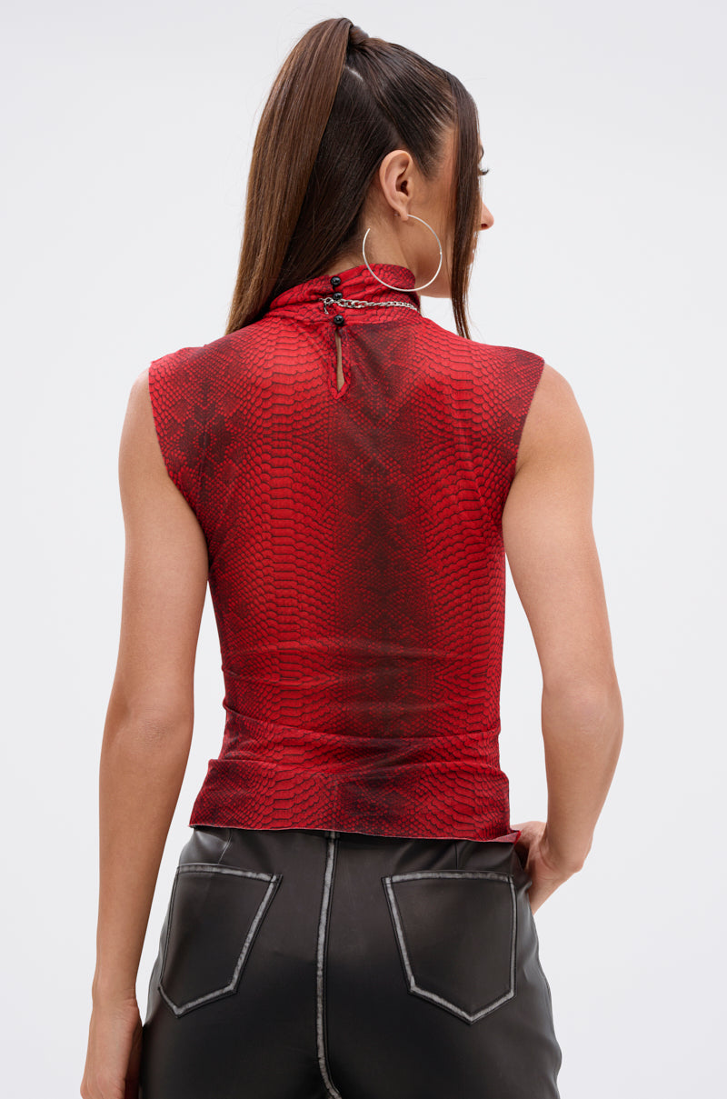 A woman with long brown hair in a high ponytail models the SEXY LITTLE SNAKE MESH TOP IN RED, paired with black leather pants, facing away from the camera against a plain light background. 4