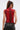A woman with long brown hair in a high ponytail models the SEXY LITTLE SNAKE MESH TOP IN RED, paired with black leather pants, facing away from the camera against a plain light background.
