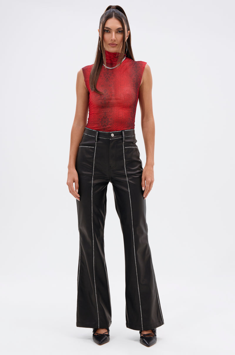 A woman poses against a plain background wearing the SEXY LITTLE SNAKE MESH TOP IN RED and high-waisted black flared pants with white side seams, paired with black pointed-toe shoes. 5