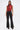 A woman poses against a plain background wearing the SEXY LITTLE SNAKE MESH TOP IN RED and high-waisted black flared pants with white side seams, paired with black pointed-toe shoes.