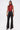 A woman with straight brown hair wears the SEXY LITTLE SNAKE MESH TOP IN RED, a sleeveless, high-neck red snakeskin top, paired with high-waisted black faux leather pants with white stitching and black pointed-toe heels against a plain white background.