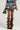 A person is wearing the OVERRATED PLAID MINI SKIRT featuring a denim trim waistband, paired with a brown textured handbag and tall, slouchy brown leather boots. The high-rise design stands out against the plain, neutral background.
