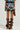 A person is wearing a blue and brown plaid dress featuring layered ruffles, capturing the charm of the OVERRATED PLAID MINI SKIRT. They pair this with tall brown button-up leather boots and carry a brown leather handbag, all against a plain gray background.